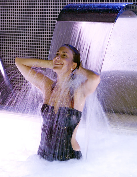 Woman under a waterfall in the Aqualux Spa of the Los Pasiegos Group